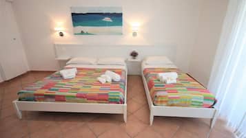 Une chambre double avec deux lits, chacun recouvert d’une courtepointe rayée aux couleurs vives et agrémenté de coussins blancs. Un tableau est accroché au mur au-dessus des lits, et deux lampes sont fixées au mur.