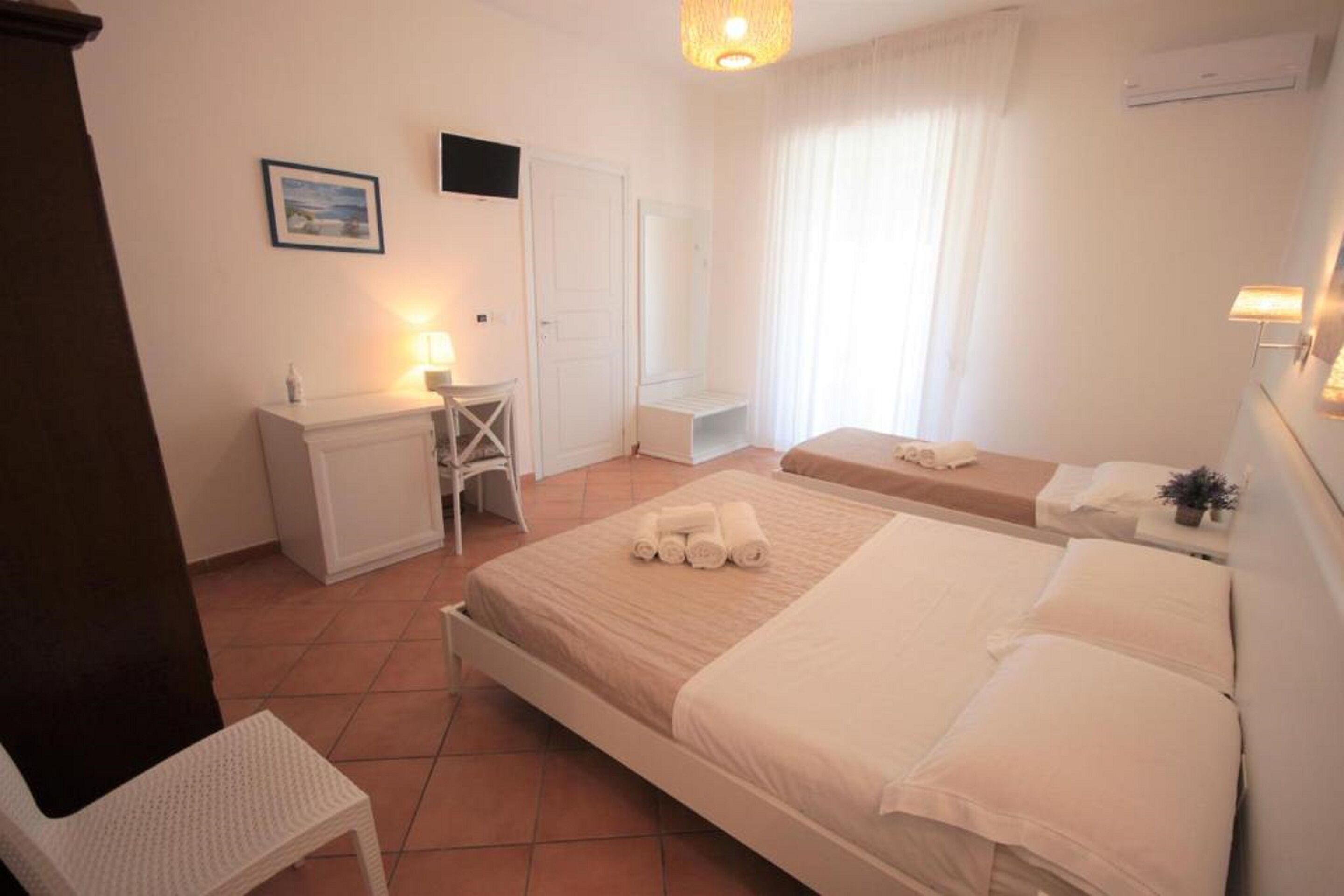 A hotel room with a bed, bedside table, desk, chair, and a window with curtains.