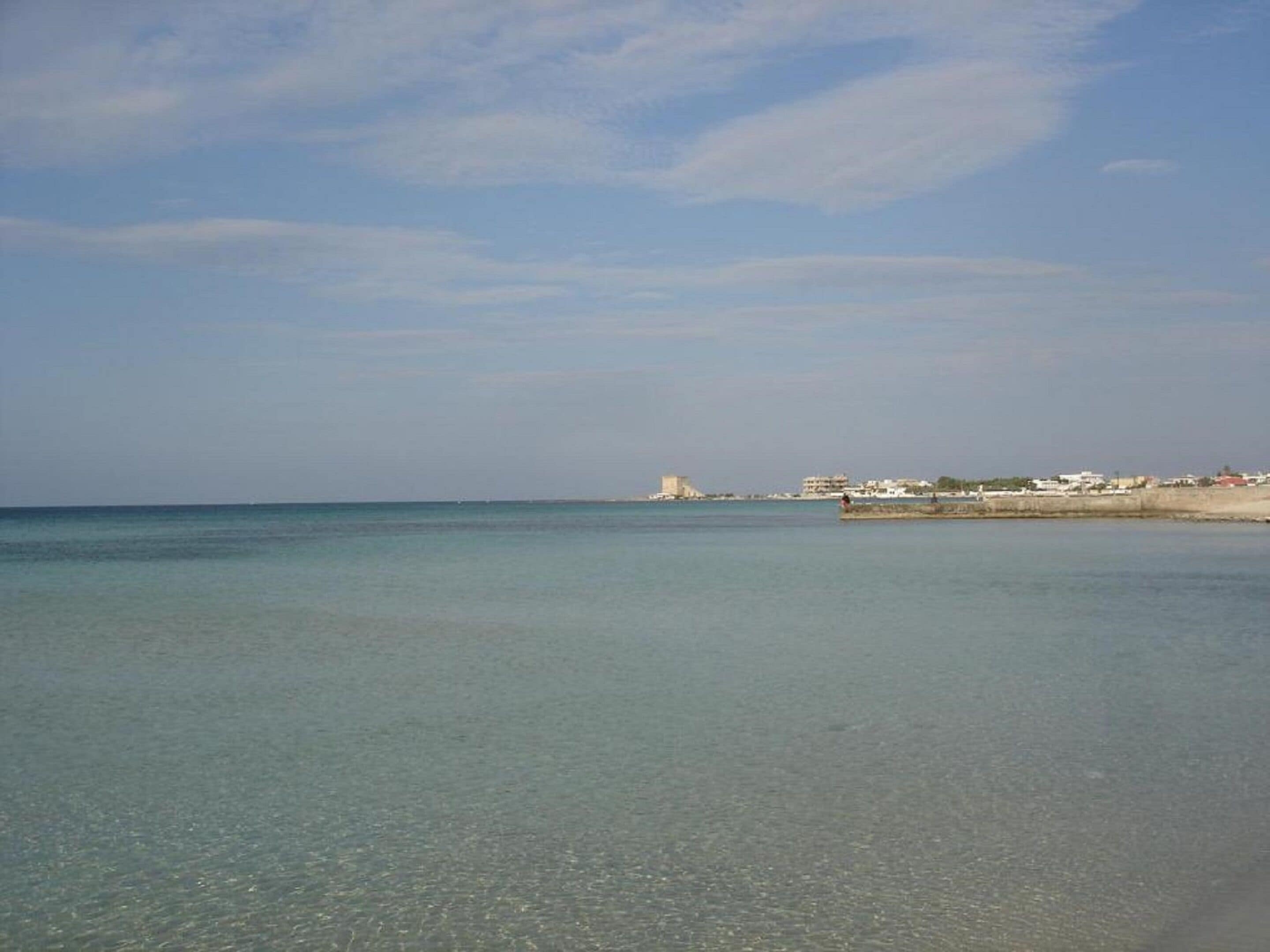 Ein Küstenstrand mit klarem Wasser und einer weit entfernten Ansicht einer befestigten Anlage.