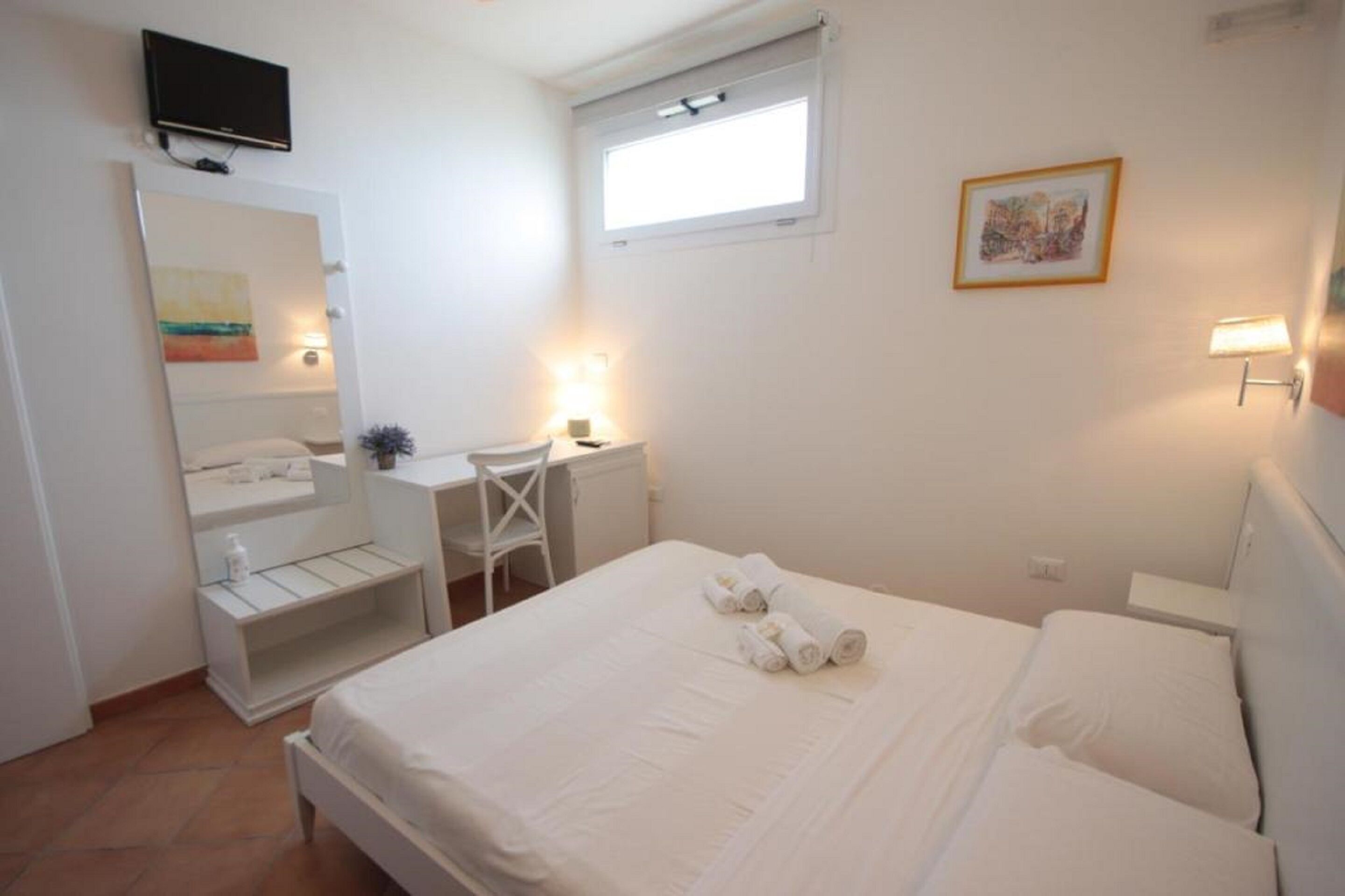 A hotel room with a bed, a desk, a chair, a TV, a window, and a painting on the wall.