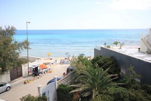 Blick auf die Küste mit Strand, Sonnenschirmen und einem geparkten Auto.