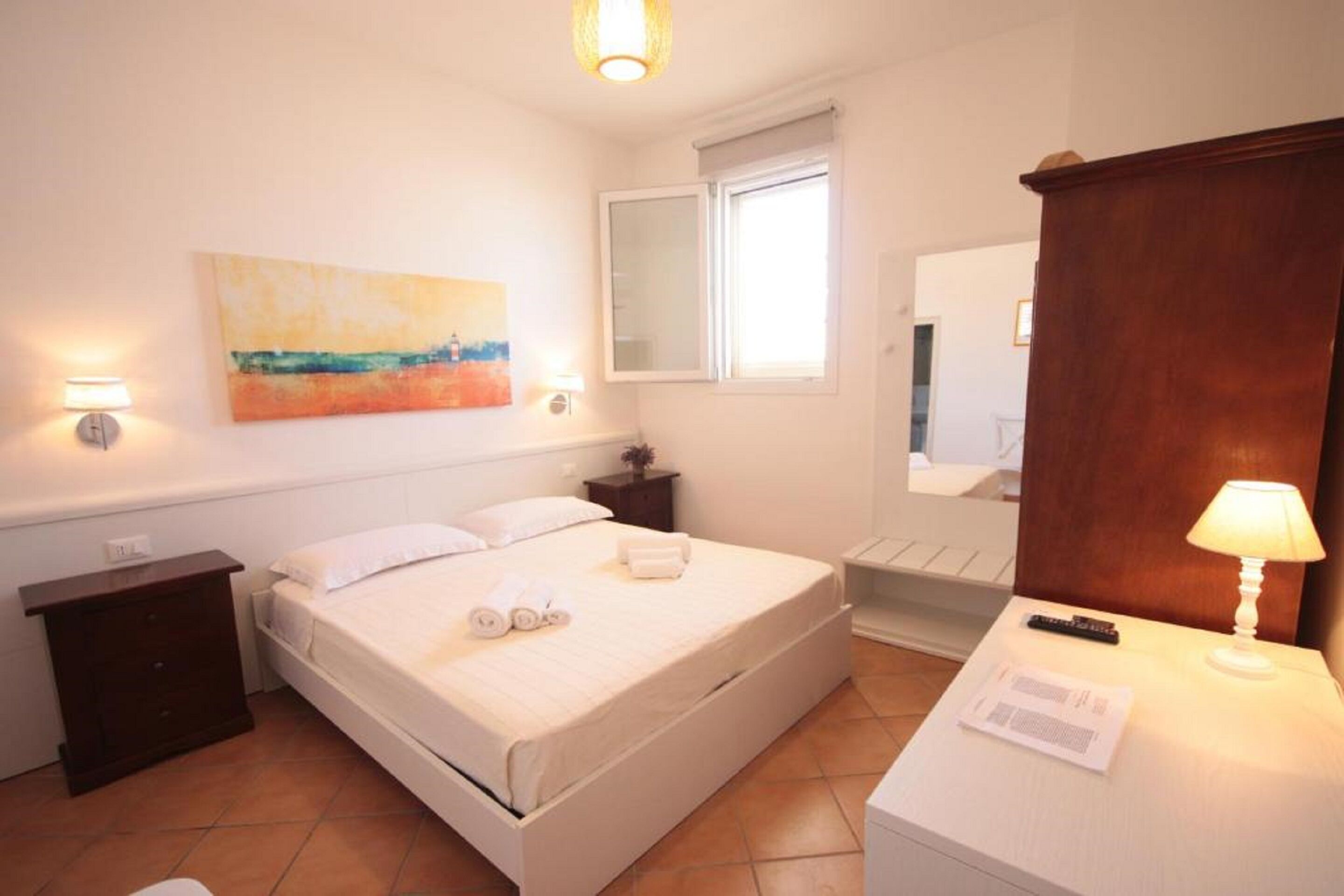 Ein Schlafzimmer mit Bett, Nachttische, Lampe, Gemälde, Fenster und Spiegel.