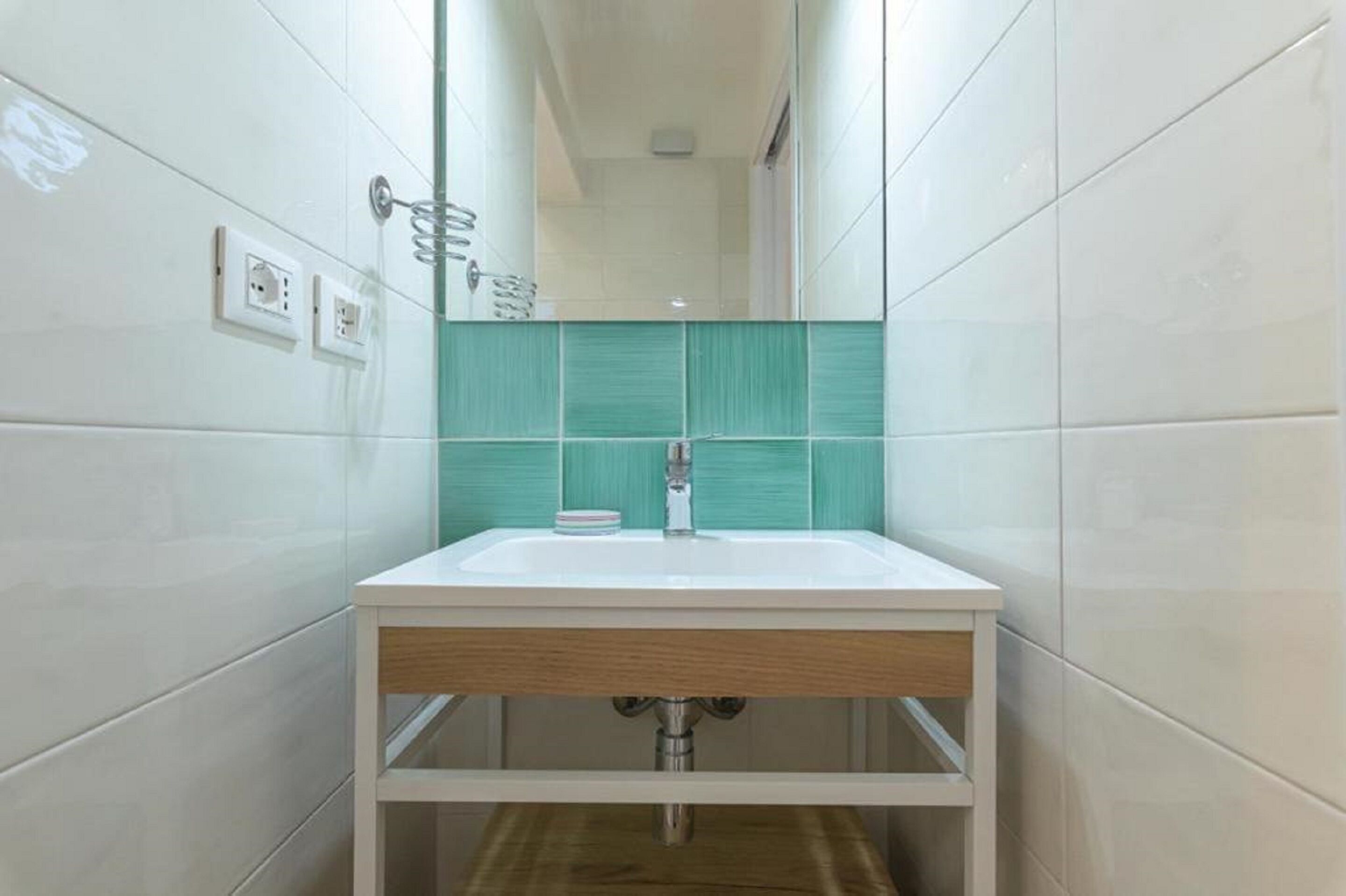 A bathroom with a white sink, green-tiled backsplash, and a wooden vanity.