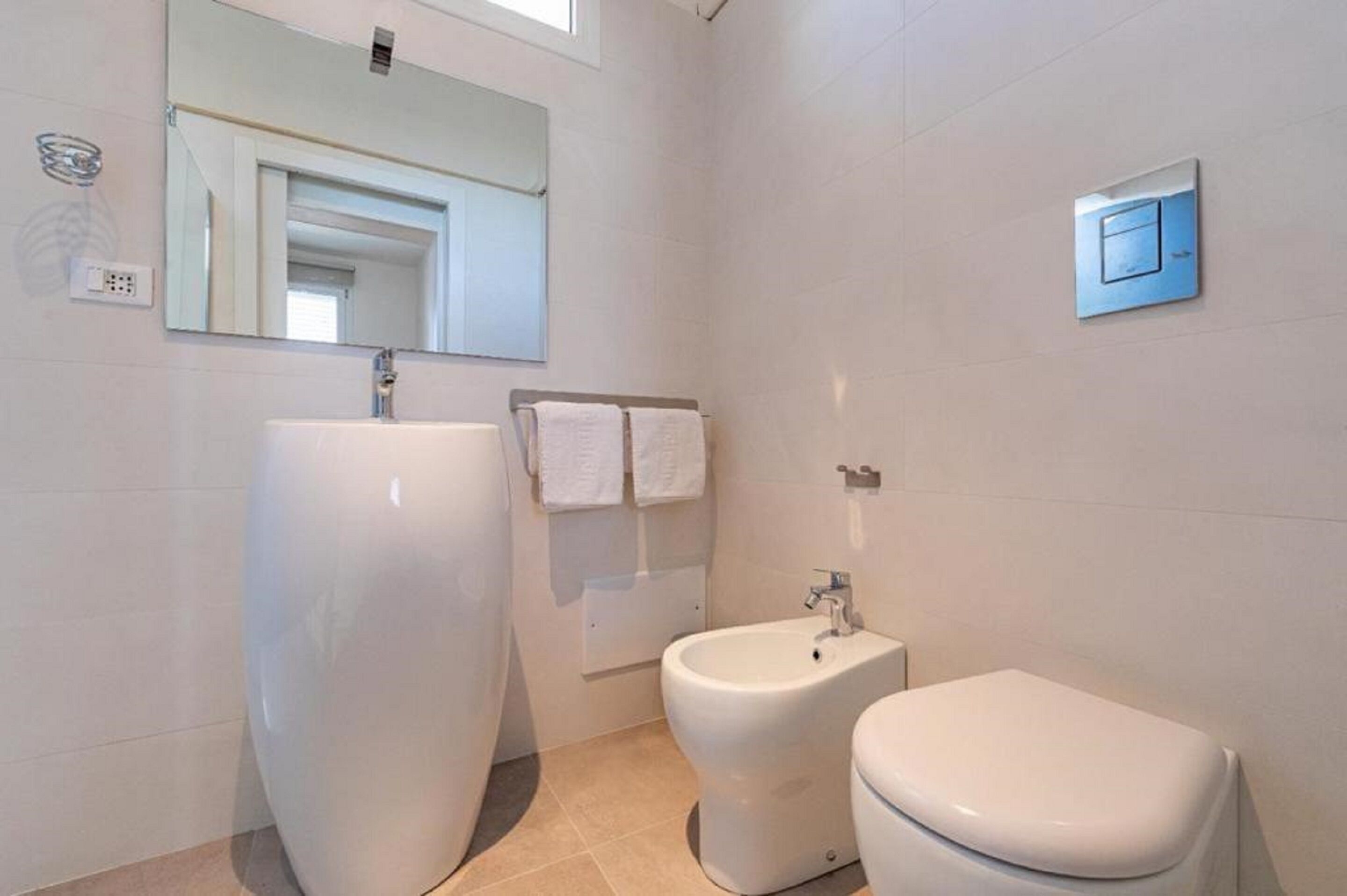 A modern bathroom with a large white sink, a bidet, and a toilet.