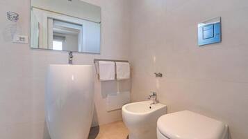 A modern bathroom with a large white sink, a bidet, and a toilet.
