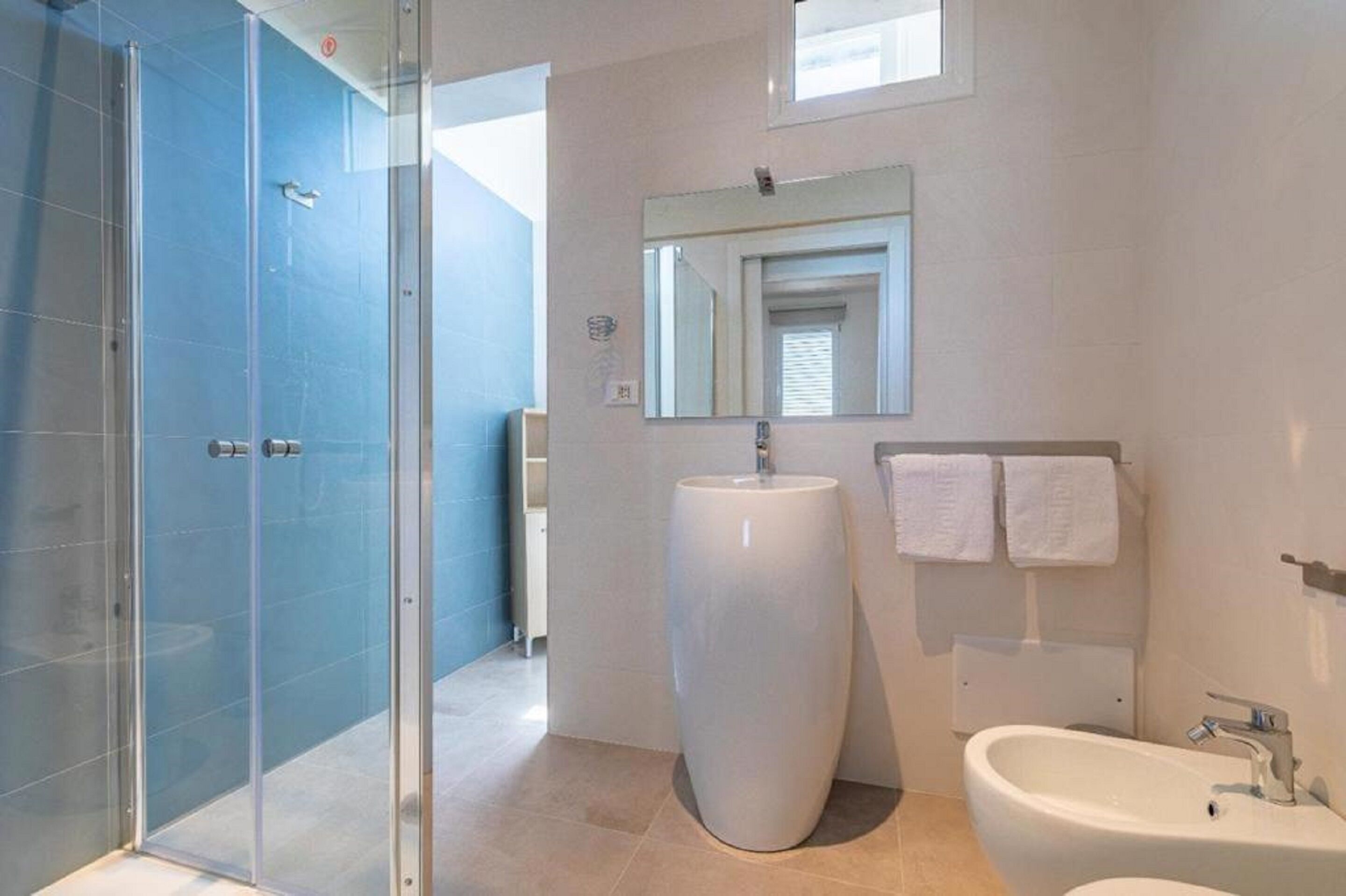 A modern bathroom with a glass shower enclosure, a large pedestal sink, and a wall-mounted mirror.