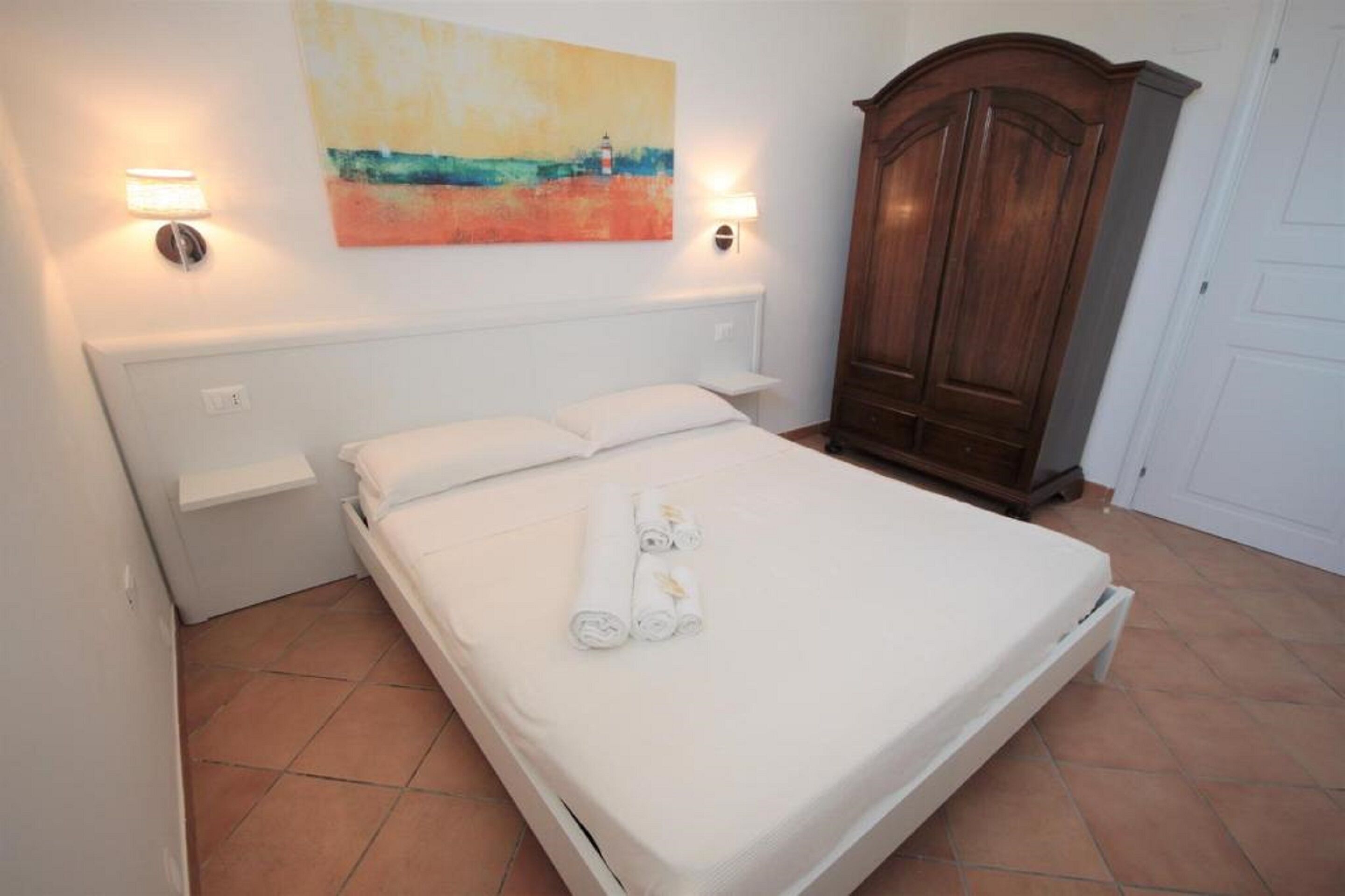 Un lit bien fait, avec du linge de lit et des serviettes blanches, une armoire en bois et un tableau accroché au mur.