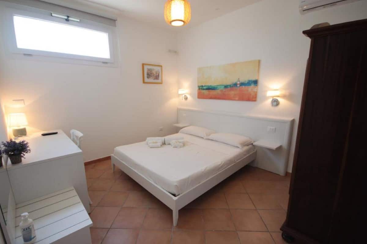 A bedroom with a bed, bedside lamps, a desk, and a wardrobe.