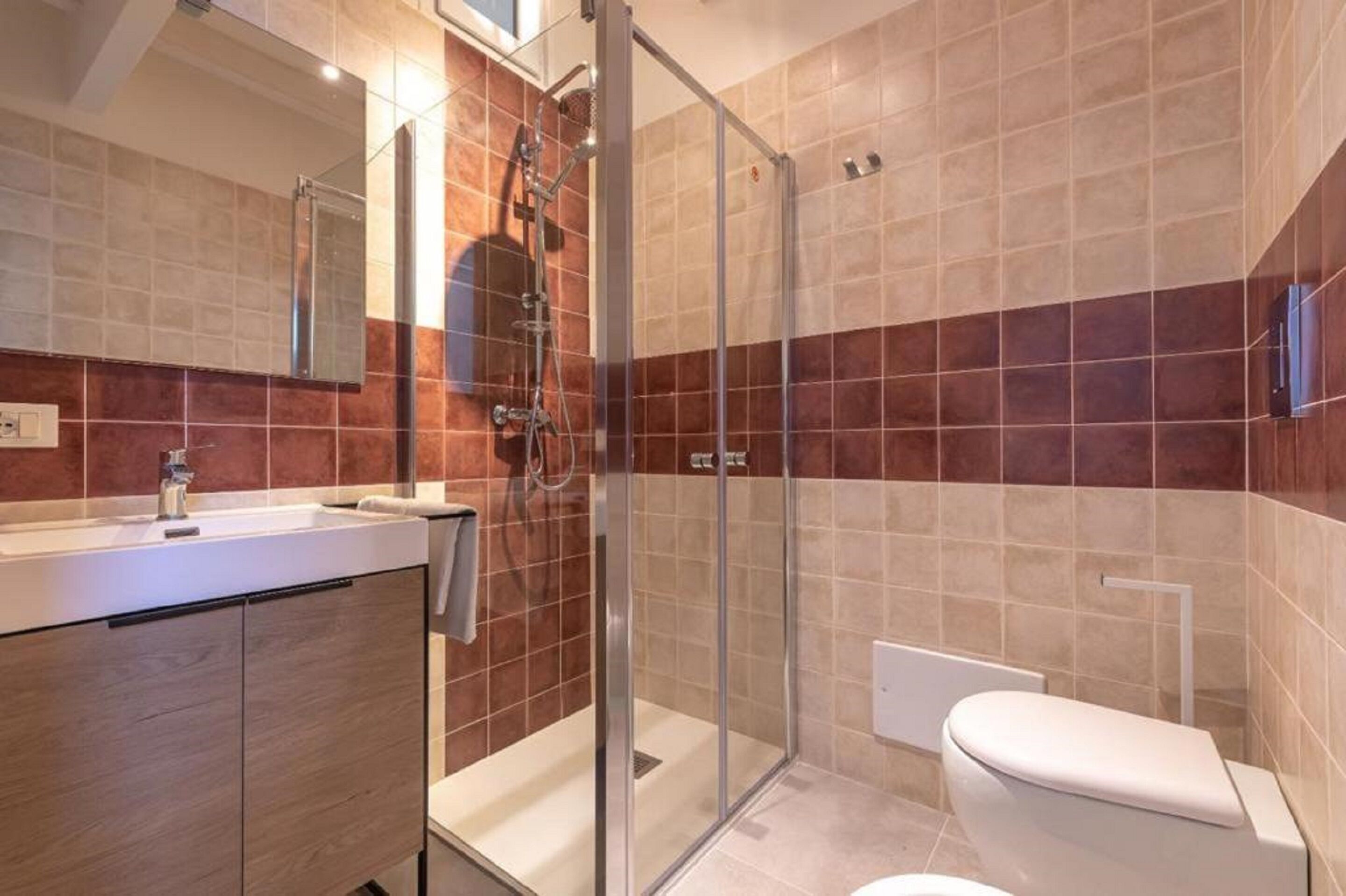 Et moderne badeværelse med bruseniche i glas, et hvidt toilet og en vask med spejl.