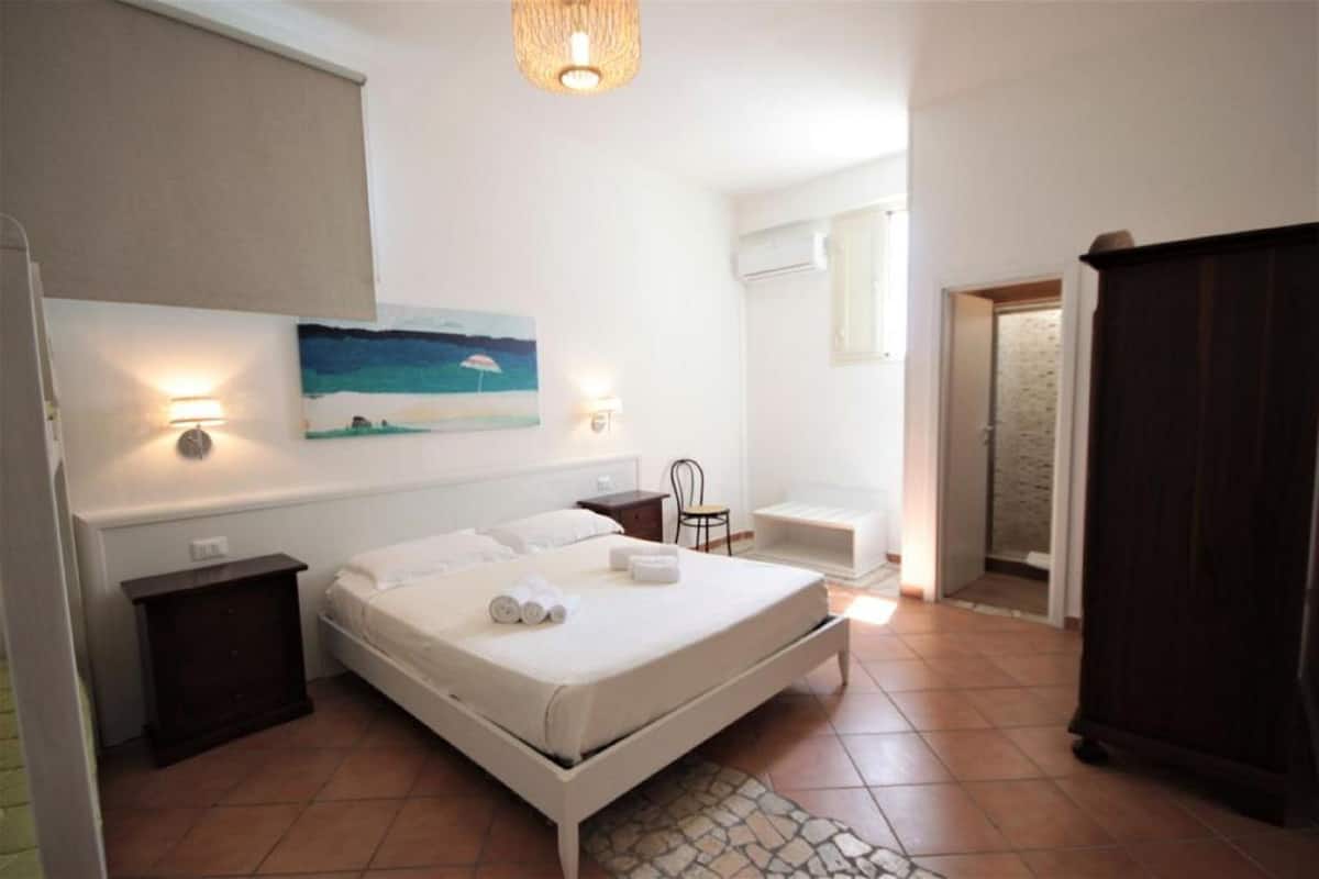 A bedroom with a bed, bedside tables, a painting, and a wardrobe.