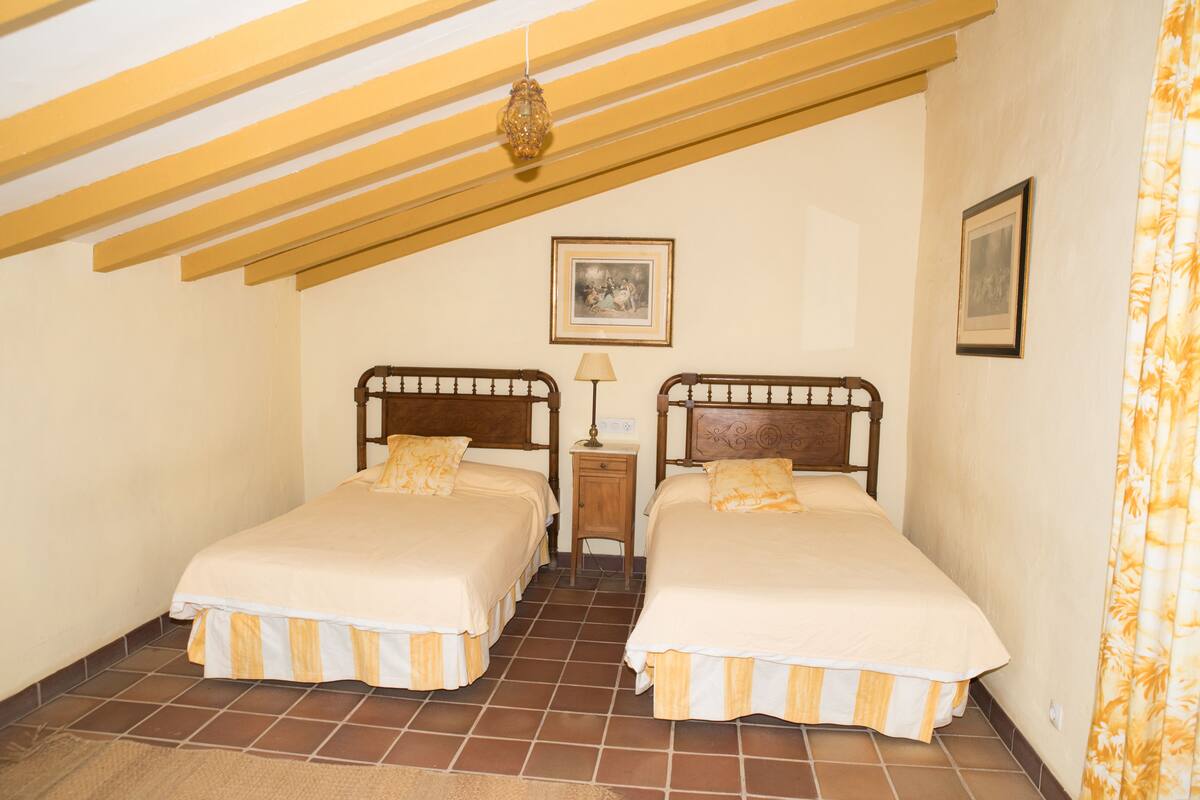 A bedroom with two beds, a nightstand, a lamp, and a framed picture on the wall.