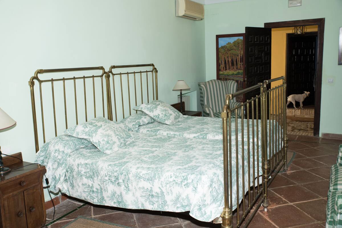 A bedroom with a bed, a chair, a lamp, and a dog near a door.