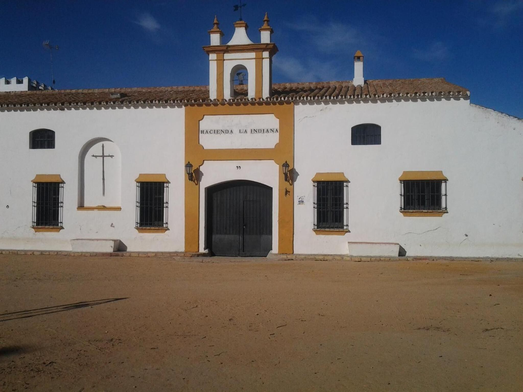 A white building with a central entrance, a bell tower, and a cross above the entrance.