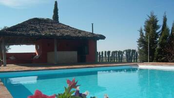 Une piscine avec une structure adjacente dotée d’un toit de chaume.
