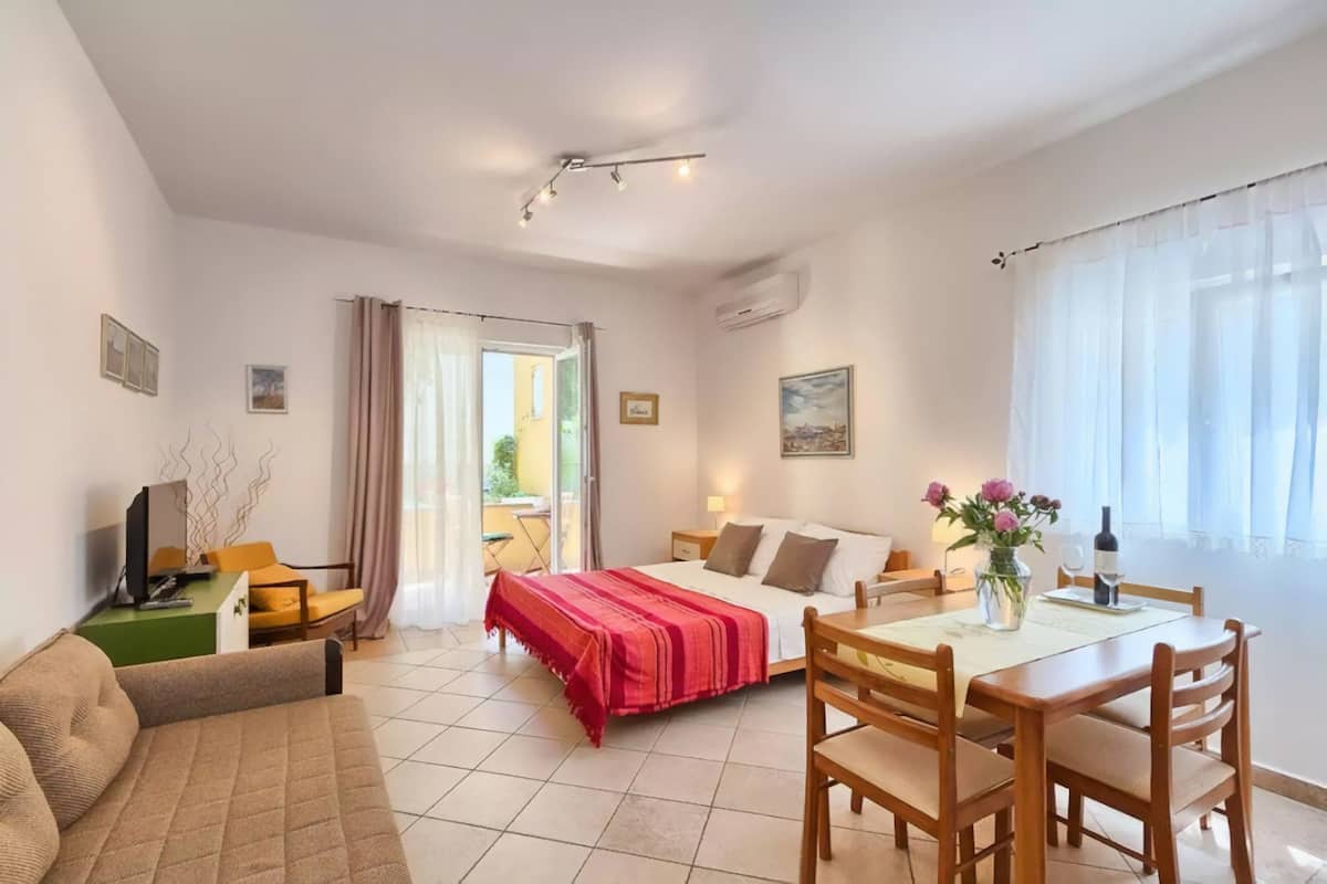 Quarto de hotel com uma cama, um sofá, uma mesa de jantar com cadeiras, uma televisão e uma janela com cortinas.
