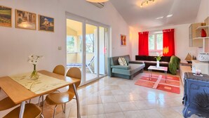 A spacious living area with a dining table, chairs, a sofa, and a coffee table. There is a sliding glass door leading to an outdoor area.