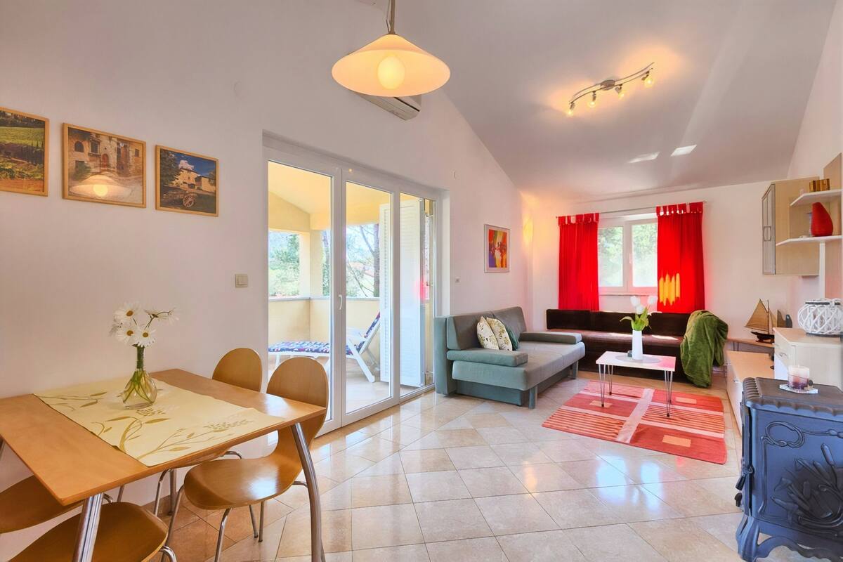Uma sala de estar ampla, com mesa de jantar, cadeiras, sofá e mesinha de centro. Há uma porta de vidro deslizante que dá para uma área externa.