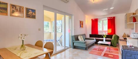 A spacious living area with a dining table, chairs, a sofa, and a coffee table. There is a sliding glass door leading to an outdoor area.