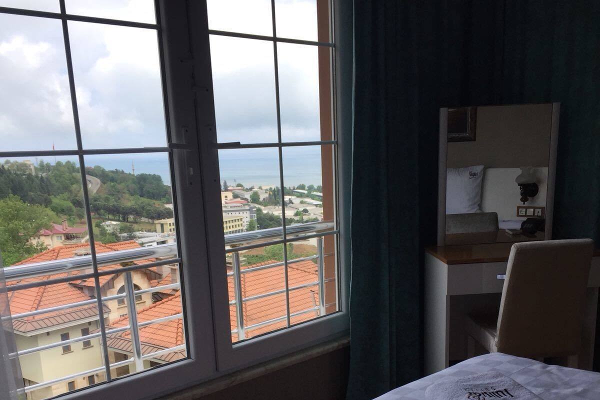 Ein Hotelzimmer mit großem Fenster und Blick auf Gebäude sowie ein Gewässer. Ein Bett, zwei Handtücher und ein Schreibtisch mit Stuhl sind vorhanden.
