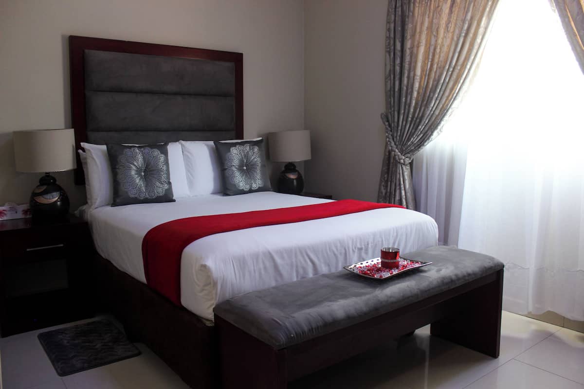 A neatly made bed with a red blanket, two bedside lamps, and a tray with a red cup and strawberries.