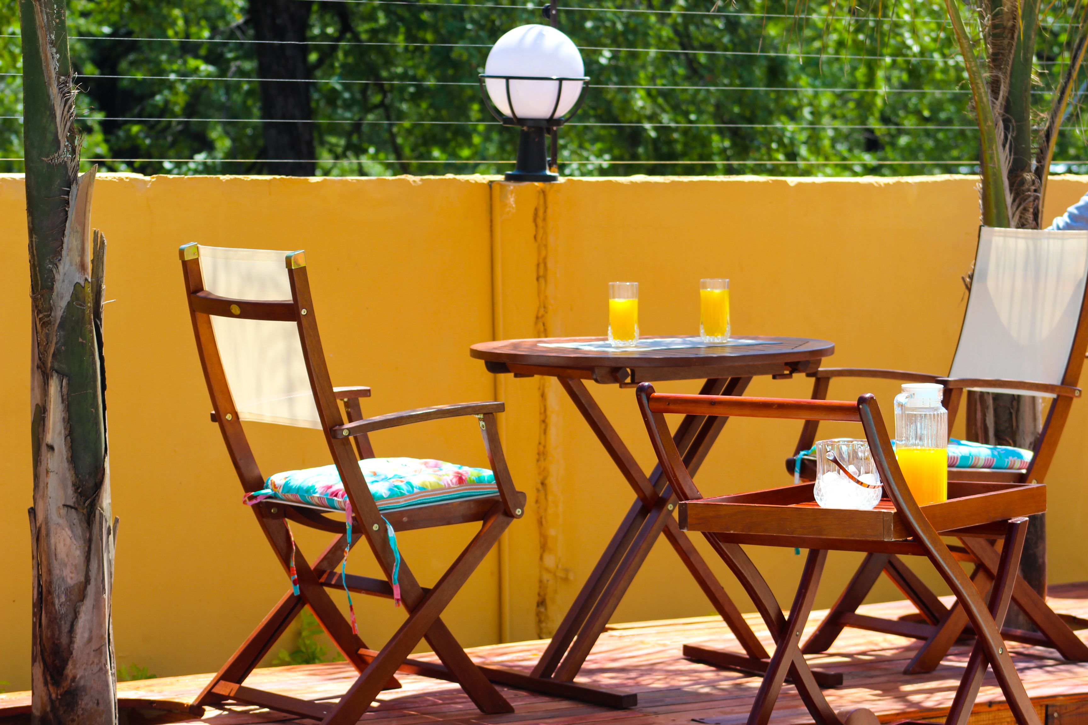 An outdoor seating area with wooden chairs and a table, featuring two glasses of orange juice.