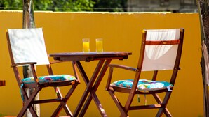 Dos sillas de madera con asientos y respaldos acolchados, una mesita redonda pequeña y dos vasos de jugo de naranja.