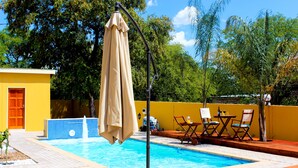 Una piscina con muelle de madera, sillones de descanso y una sombrilla.
