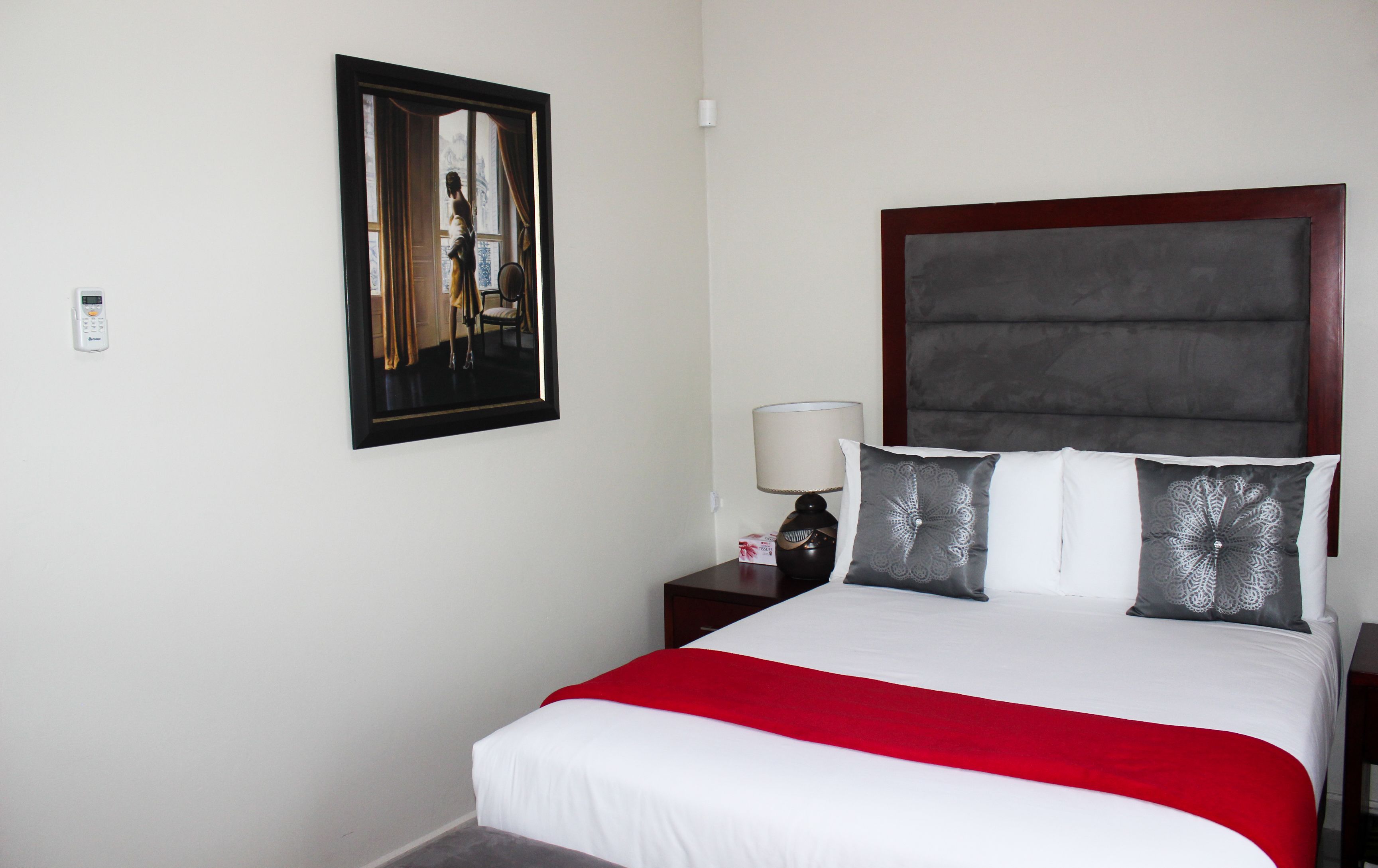 A hotel room with a bed, a nightstand, a lamp, a framed picture, and a red throw blanket.