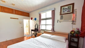 A bedroom with a large bed, wooden headboard, a window with curtains, a bedside table with a lamp, and a wall-mounted air conditioner. - YoYo MaAn B&B (Liuqiu)
