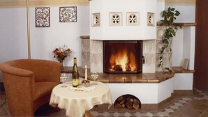 Una habitación acogedora con chimenea, una mesa con una botella y copas, una silla y decoración en la pared.