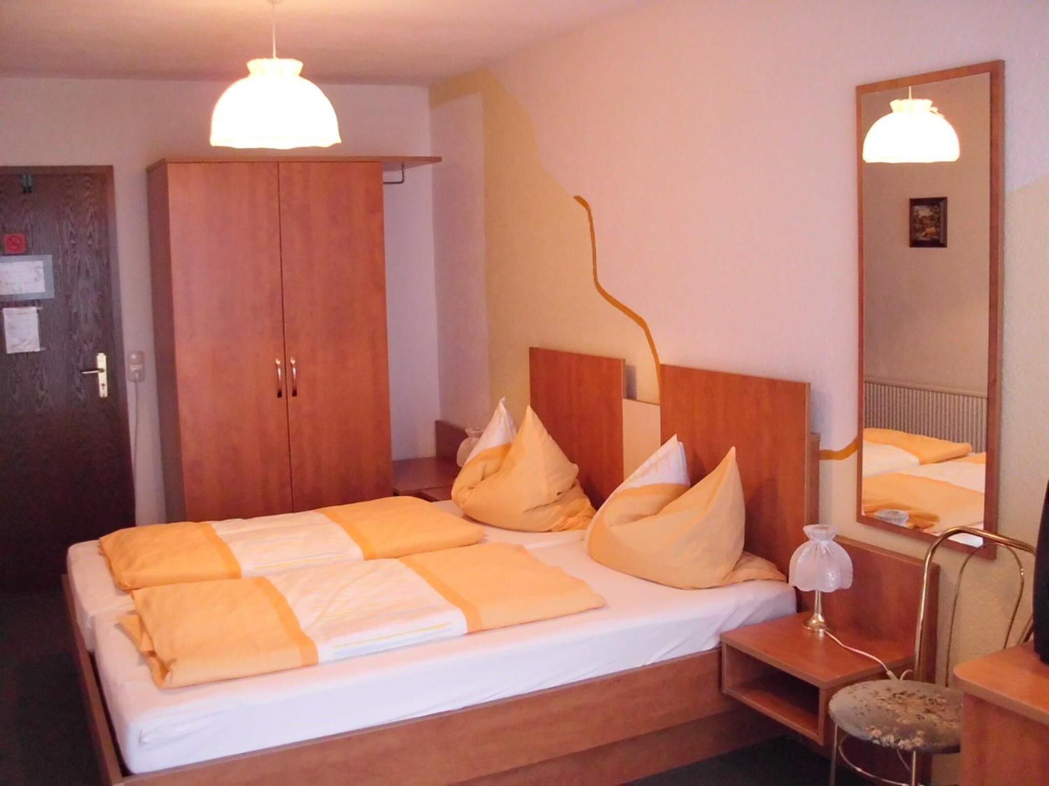Habitación de hotel con una cama grande, armario de madera, mesita de noche con lámpara y un espejo en la pared.