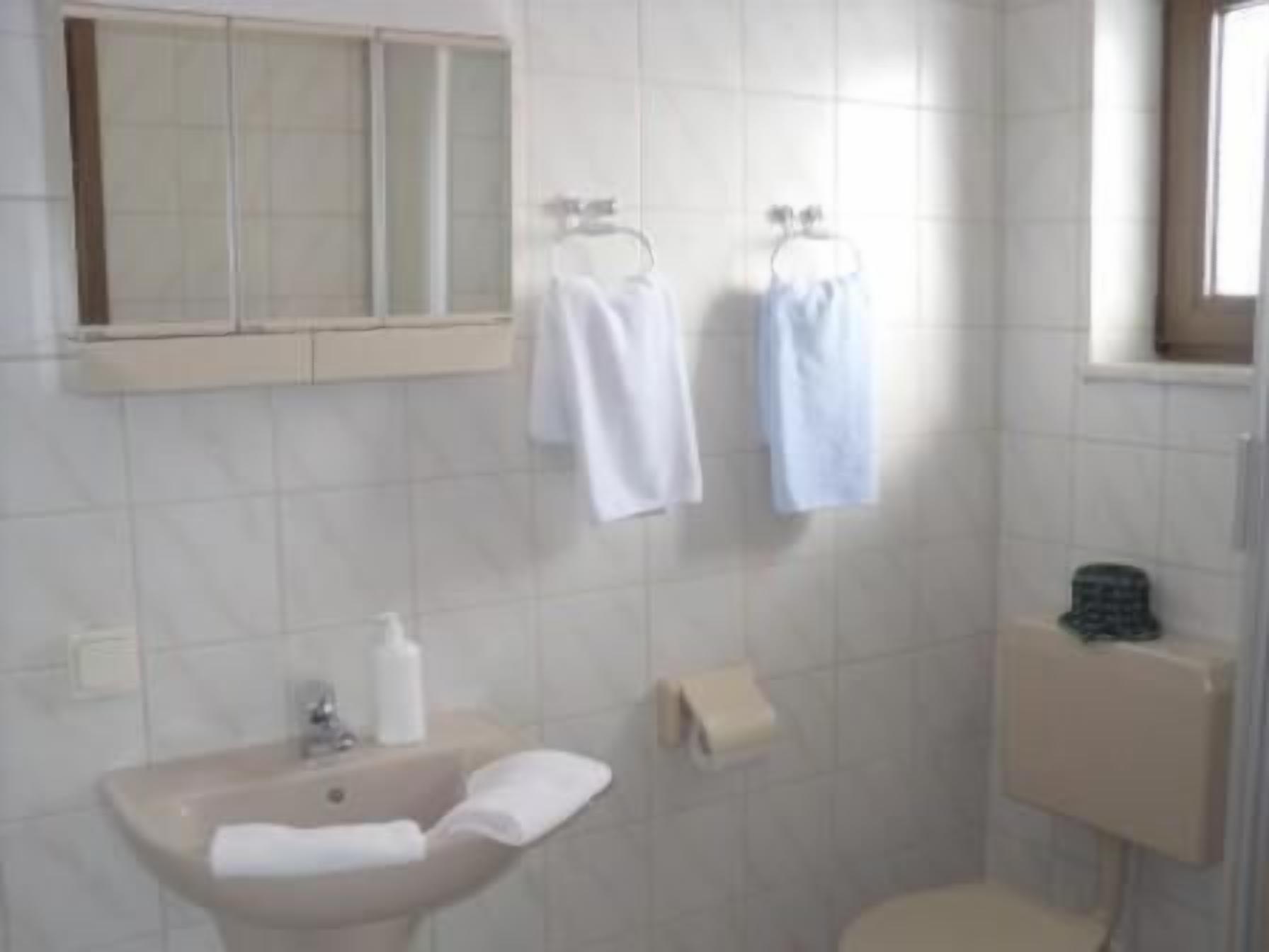 A bathroom with a sink, mirror, towel rack, toilet, and a window.