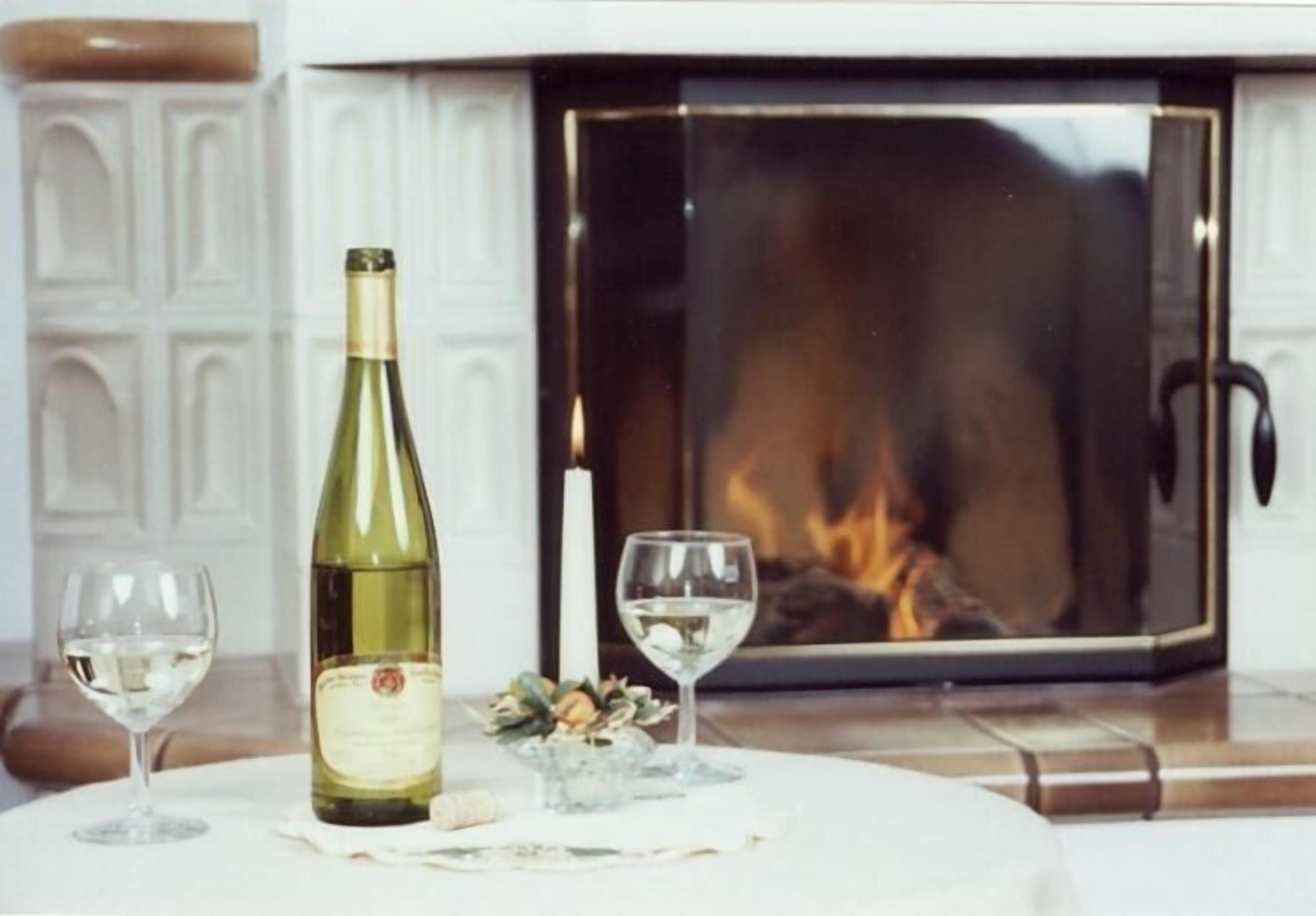 A fireplace with a lit fire, a wine bottle, and two wine glasses on a table.