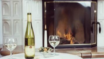 A fireplace with a lit fire, a wine bottle, and two wine glasses on a table.