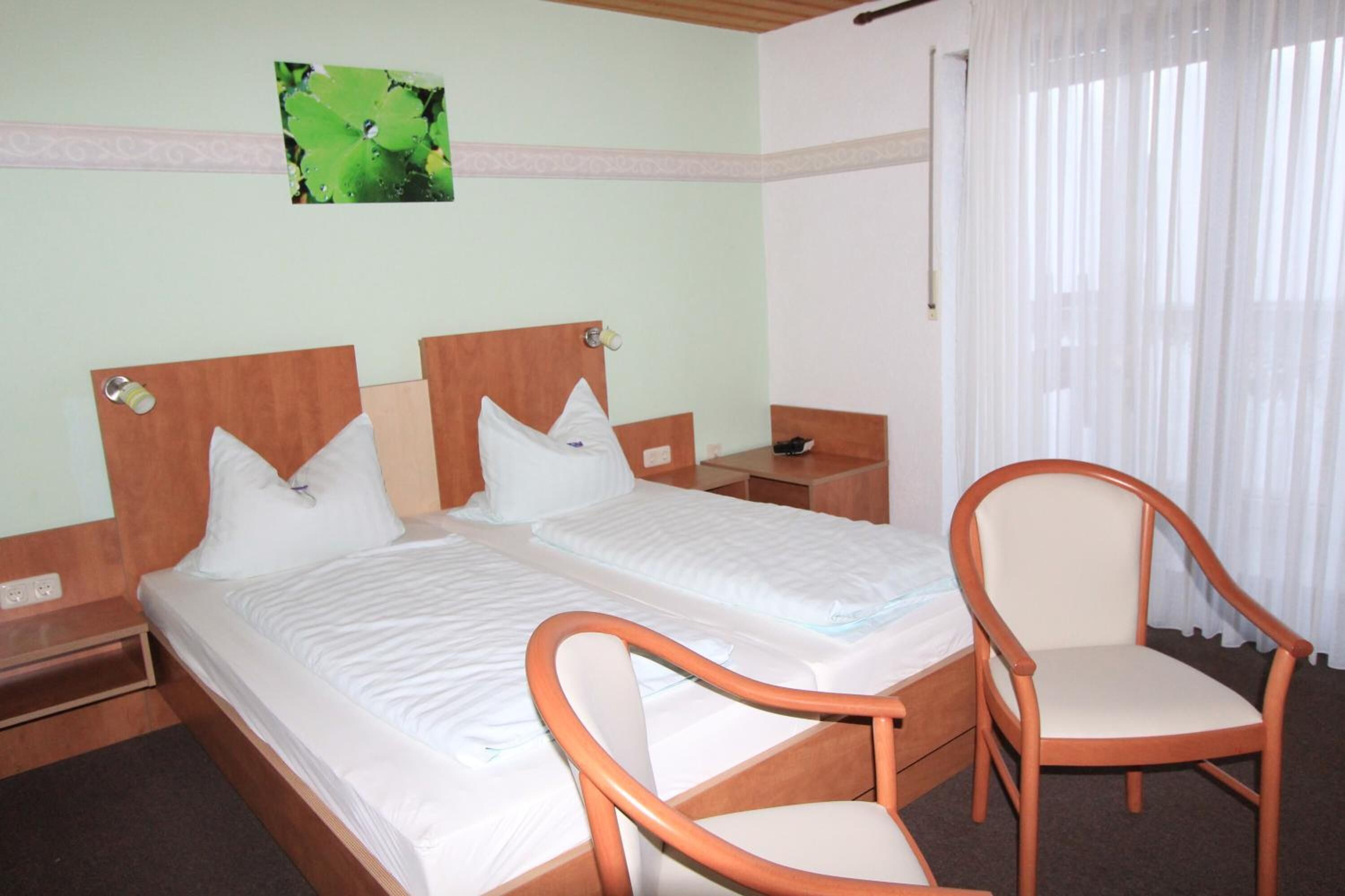 A hotel room with two beds, a wooden chair, and a nightstand.