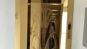 Ascensor con puertas metálicas ornamentadas y suelo de mármol.