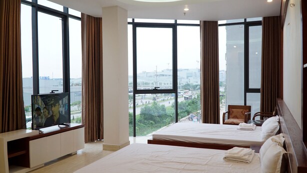 Habitación de hotel con dos camas, un televisor sobre un mueble y amplias ventanas con vistas a la ciudad.