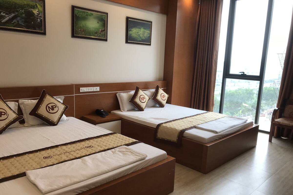 A hotel room with two beds, a nightstand, and a window with a view.