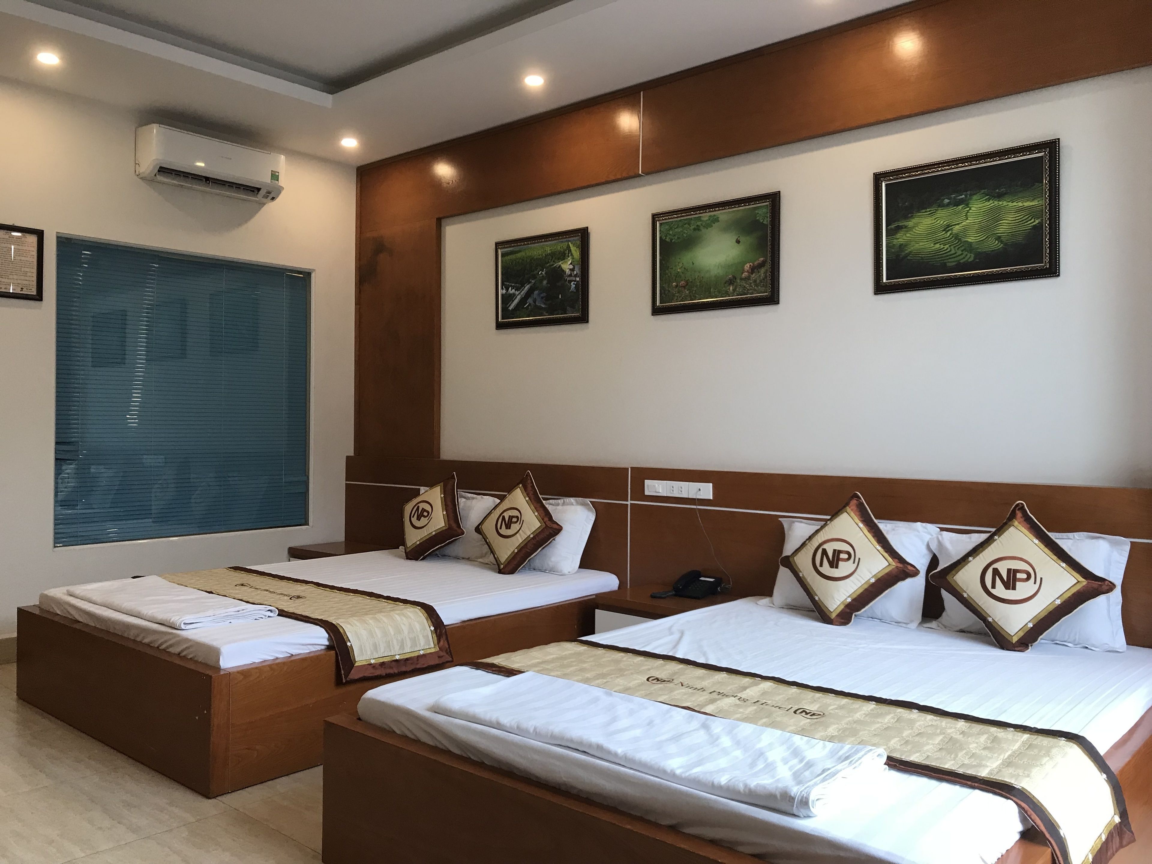 Habitación de hotel con dos camas, un ventanal con persianas y tres cuadros en la pared.