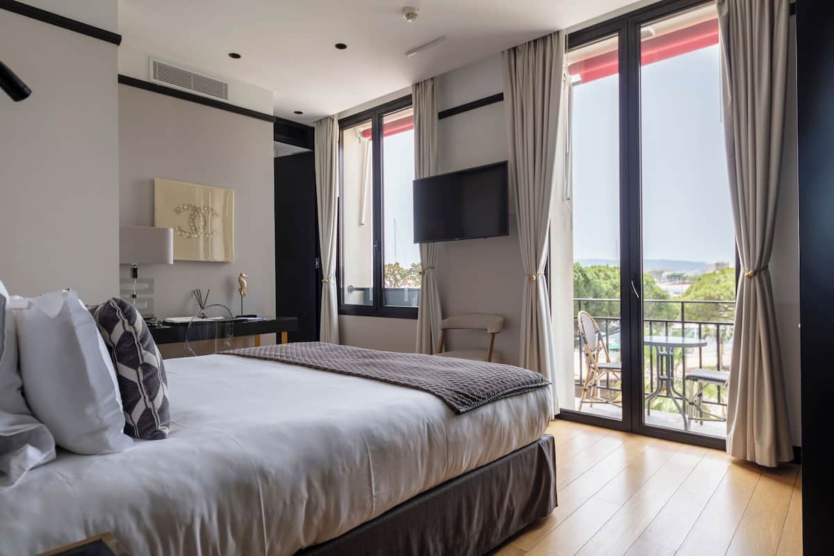 A modern bedroom with a large bed, a desk, a chair, and a balcony with outdoor furniture.