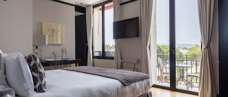 A modern bedroom with a large bed, a desk, a chair, and a balcony with outdoor furniture.
