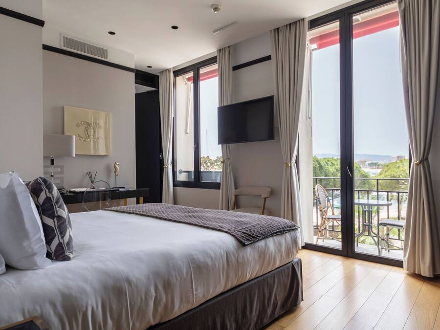 Een moderne slaapkamer met een groot bed, een bureau, een stoel en een balkon met tuinmeubilair.