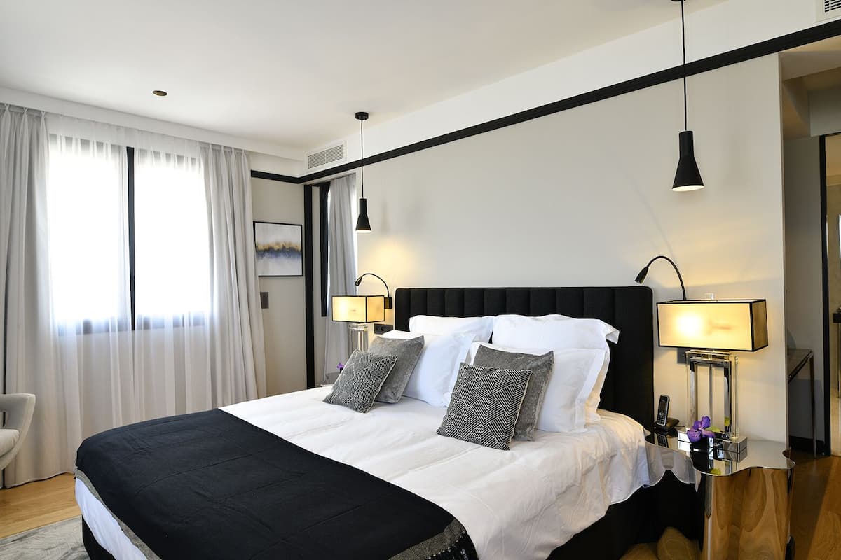 A modern hotel room with a large bed, black and white bedding, two bedside lamps, a nightstand, and a chair.