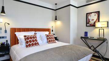 A modern hotel room with a large bed, a desk, and a wall-mounted artwork.