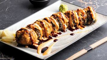 Un plato de sushi sobre una bandeja rectangular, con palillos y un pequeño tazón de salsa.