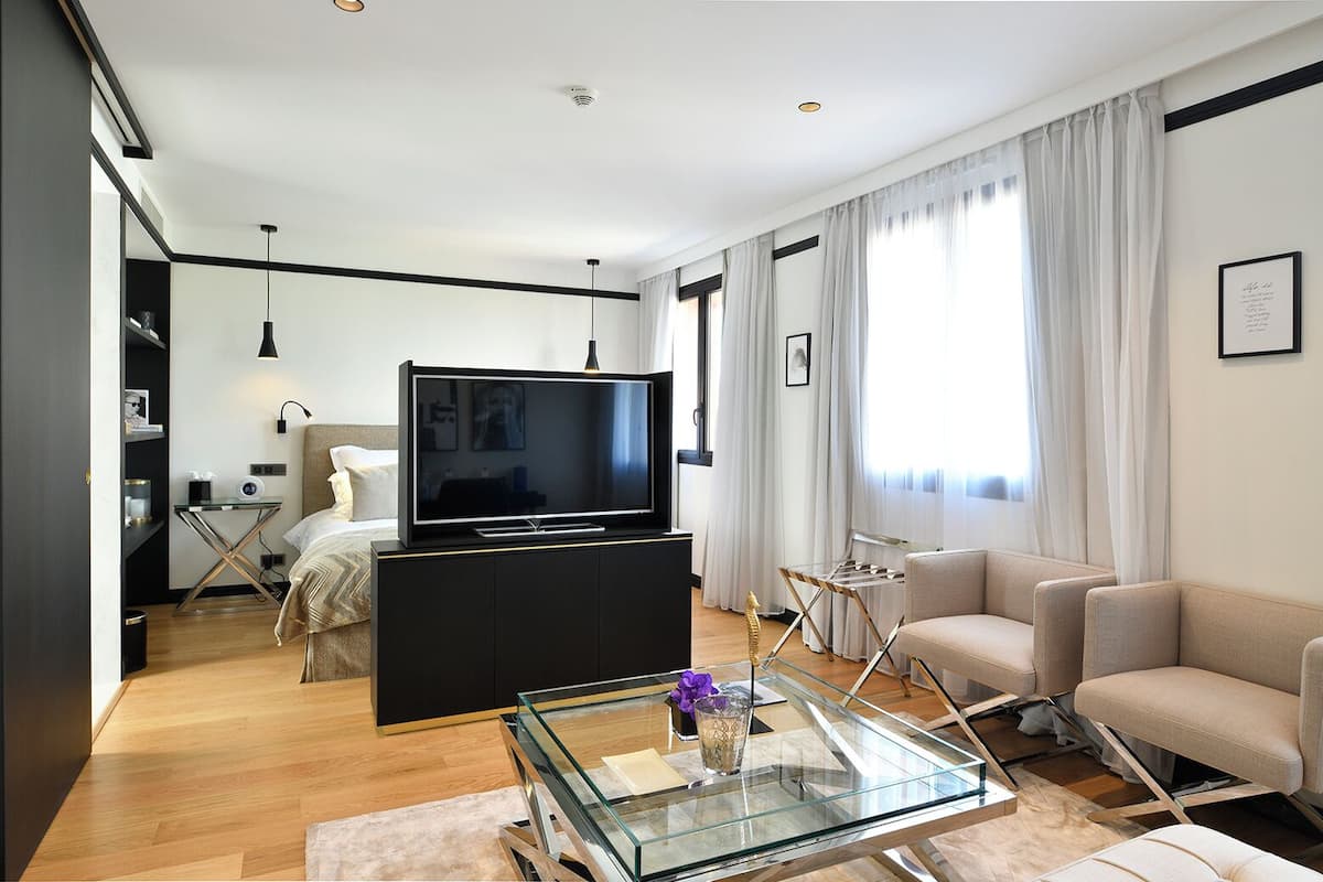 A modern living room with a flat-screen TV, a glass coffee table, a sofa, and a dining area with a glass table.
