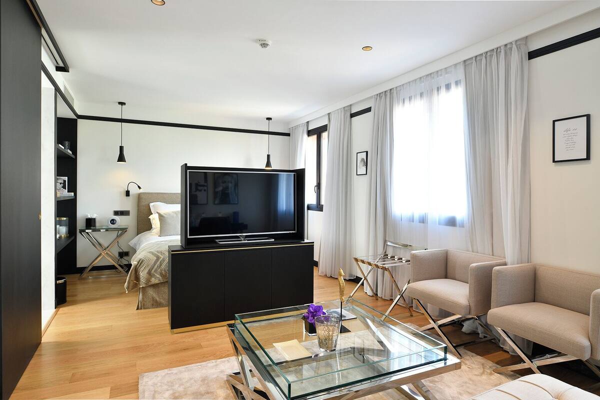 A modern living room with a flat-screen TV, a glass coffee table, a sofa, and a dining area with a glass table.