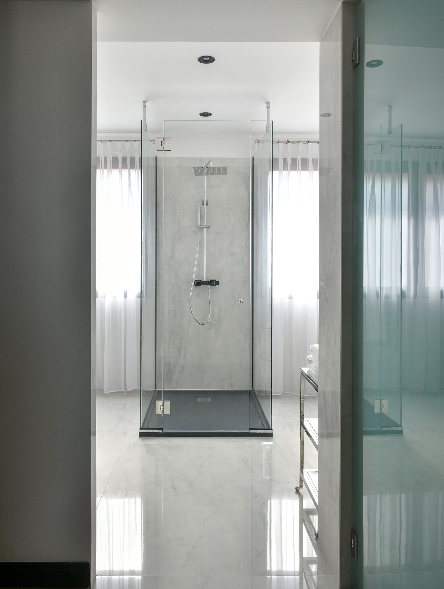 Ein modernes Badezimmer mit einer gläsernen Duschkabine, weißen Marmorwänden und einer Glastür.