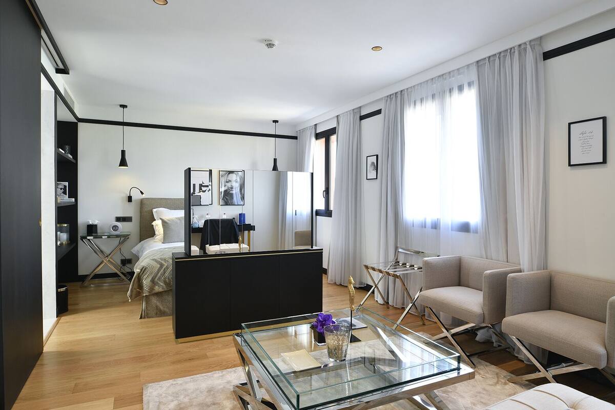 A modern living room with a glass coffee table, a sofa, a bed, and a desk area.