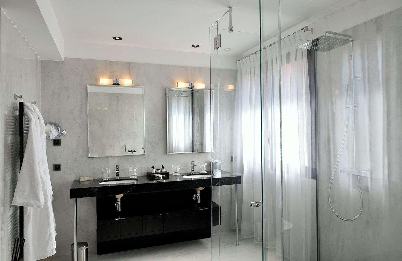 Un baño moderno con dos lavamanos, un espejo grande y una ducha con cerramiento de vidrio.